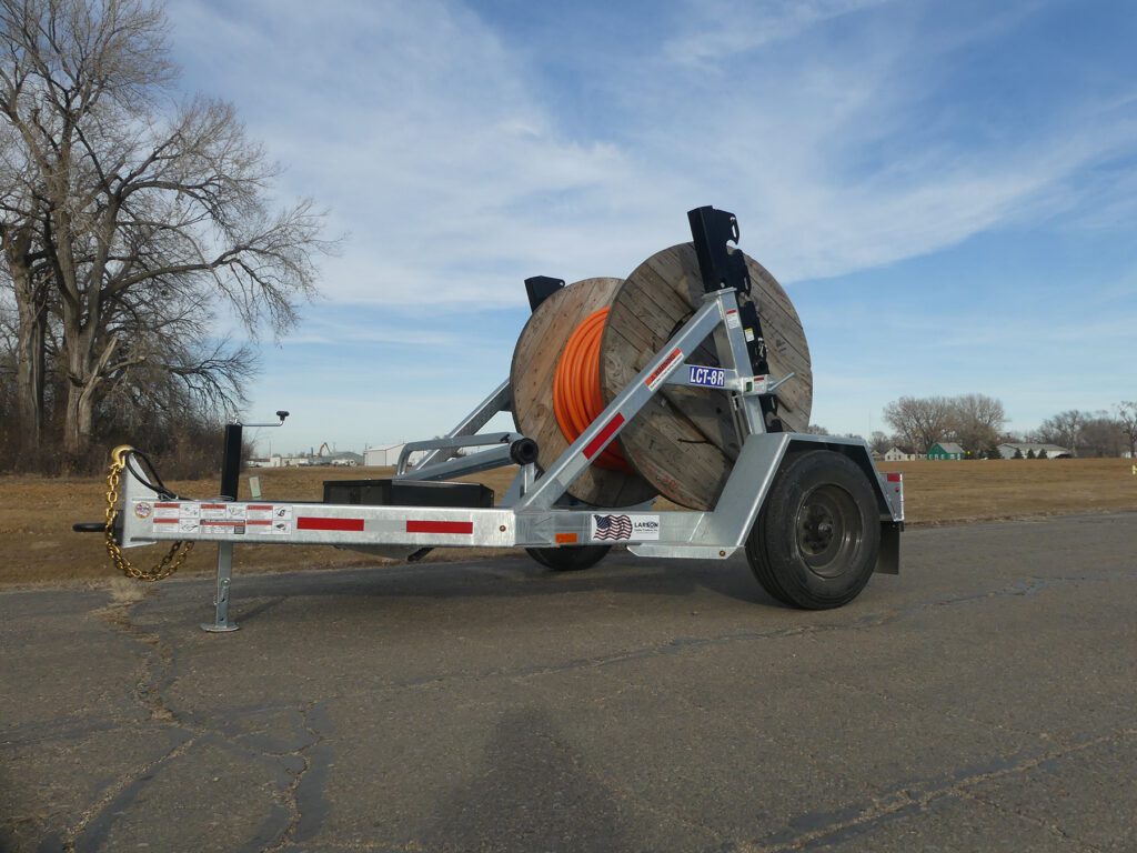 A pair of heavy-duty utility trailers for cable installation, the Larson LCT 7500 and LRT 8R Combo, outdoors.